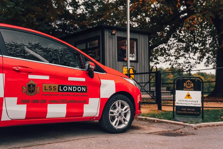 LSS London security patrol car beside a gated site entrance with CCTV monitoring sign and security cabin.