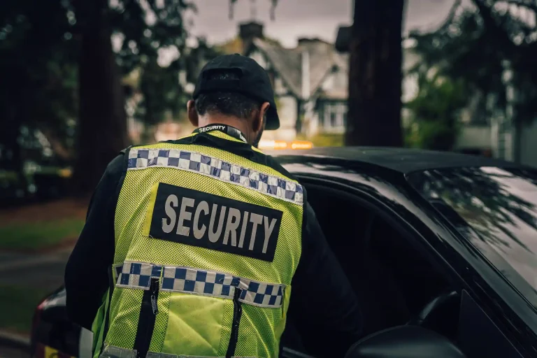 Security guard in high-vis vest marked “SECURITY” opening a car door.